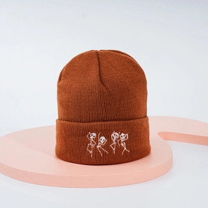 Détail du bonnet en tricot caramel montrant des broderies de squelettes dansant sur tissu côtelé