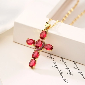 Close-up of a gold cross pendant with red zircons and pink gemstones on a chain