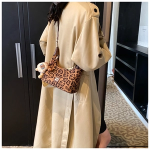 Close-up of leopard print shoulder bag with plush lion charm on a beige trench coat