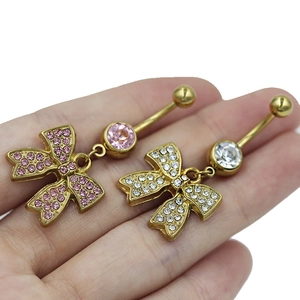 Macro shot of two golden bow belly rings with pink and white rhinestones on white background
