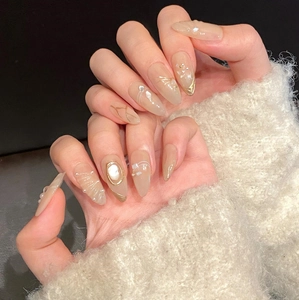 Detailed close-up of nude almond press-on nails with gold lines, pearls and crystal accents