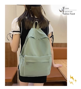 Detail view of a light green nylon backpack featuring a spacious front zipper pocket