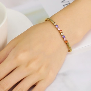 Detail of a gold spring bracelet set with colorful round-cut zircons worn by a model