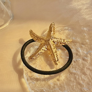 Golden starfish metal hair tie with hammered texture on minimalist black elastic band