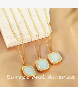 Three gold chain necklaces with square light blue gemstones on a beige stone
