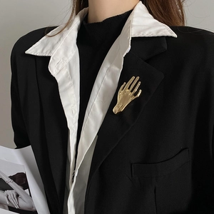 Detailed view of a golden palm-shaped brooch on a black suit jacket for elegant styling