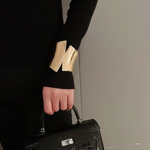 Close-up of a wide irregular golden cuff bracelet styled over a black sleeve