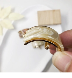 Gros plan d'une boucle d'oreille en acétate en C avec base dorée et motif marbre