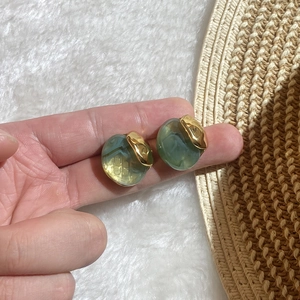 Handheld view showing green and amber oval resin earrings with gold accents