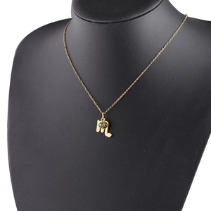 Detail of gold Scorpio zodiac necklace with green birthstone on black mannequin