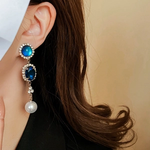 Dettaglio di orecchino vintage con pietre blu e un ciondolo di perla bianca