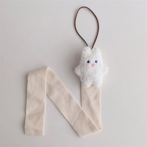 Close-up of a white plush rabbit charm with beige herringbone ribbon and hanging loop