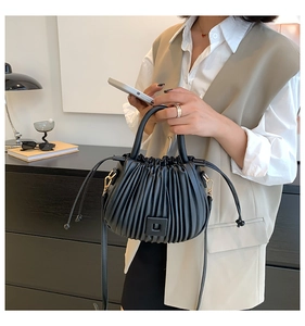 Detail of black pleated bucket bag with magnetic closure and crossbody strap on a model