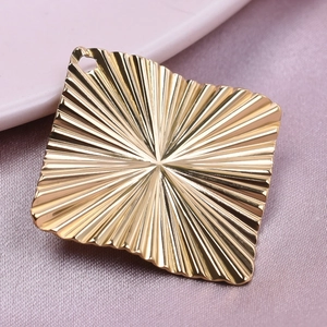 Detailed view of golden diamond-shaped pendant with radial wave patterns and top hole