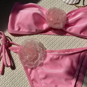 Detailed flat lay of pink shiny bikini with 3D organza flowers and side-tie bottom