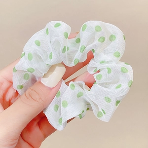 Detail shot of a white scrunchie with green polka dots held by a hand on beige background