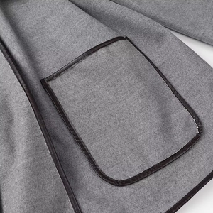 Detailed macro view of gray wool coat featuring black leather trim on a large patch pocket