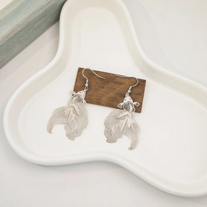 Macro detail of silver fish-shaped hollowed earrings on a wooden stand