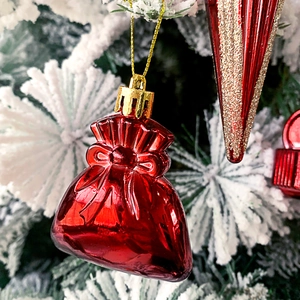 Nahaufnahme eines roten Glücksbeutel-Anhängers mit Schleife am verschneiten Tannenbaum