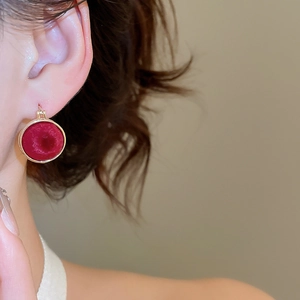 Close-up of elegant red velvet round earrings with gold trim worn by a model