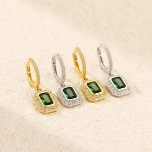Macro detail of gold and silver earrings featuring emerald green stones and pavé zircons