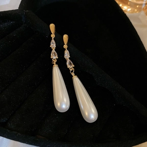 Detailed close-up of gold dangle earrings with teardrop zirconia and elegant white pearls