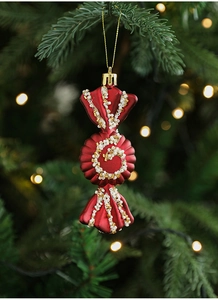 Detail of candy-shaped burgundy Christmas ornament with white beads hanging on a tree