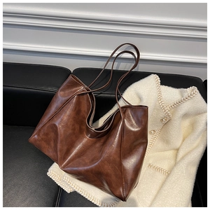 Detail of soft brown faux leather tote bag on black bench with knit cardigan