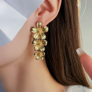Close-up of model wearing gold vintage flower tassel earrings with metallic texture