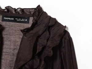 Detail of coffee brown shirt showing layered ruffle design and branded neck label