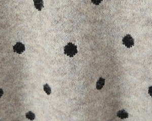Vista macro del tessuto in lana lavorata a maglia beige con motivo a pois neri classici