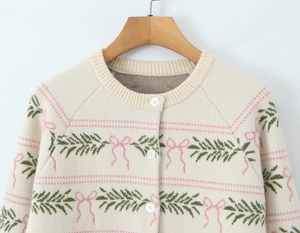 Detail of knit cardigan with pink ribbon patterns and white buttons on cream fabric