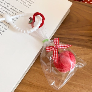 Detail of red apple pendant with wave bead lanyard and red plaid bow in clear bag