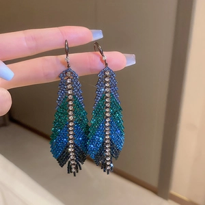 Detail of long feather drop earrings featuring blue and green gradient rhinestones
