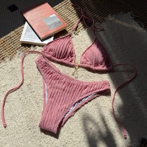 Detail of pink textured bikini with starfish pearl charms and golden ring on straw mat