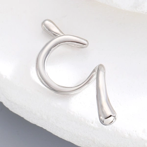 Macro detail of a minimalist silver snake-style ear cuff on a white stone background