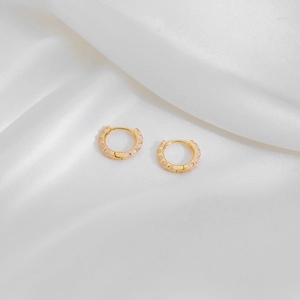 Detail of gold hoop earrings with pink enamel polka dots on a white silk background