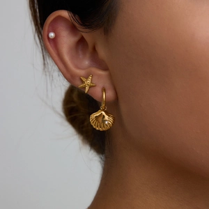 Detail of gold starfish, shell with diamond, and pearl earrings worn by a model