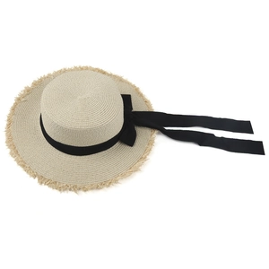 French style straw sun hat with black ribbon bow and fringed brim on white background