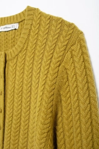 Detail of mustard yellow chunky knit cardigan showing cable texture and neck brand label