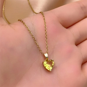 Close-up of a heart-shaped yellow zircon pendant on a gold chain held by hand