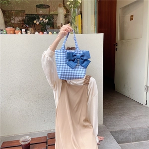 Detailed close-up of blue plaid lunch bag with a large denim bow held by a model