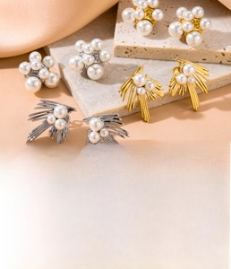 Close-up of pearl stud earrings in gold and silver finish on a textured stone surface