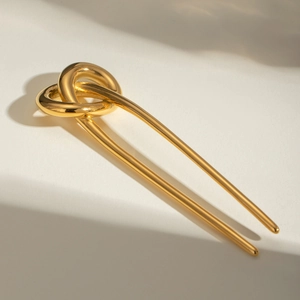 Detail of a U-shaped gold metal hair pin featuring a stylish double love knot design