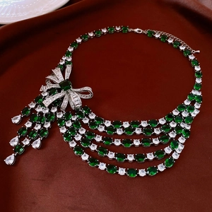 Macro detail of silver bow necklace with green gemstones and elegant layered tassels