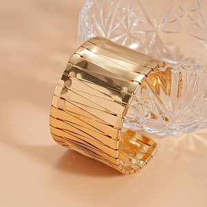 Detailed close-up of wide golden cuff bracelet with irregular geometric textured surface