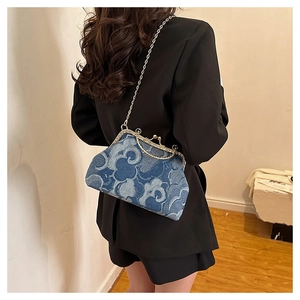 Detail of denim handbag with cloud patterns and silver chain strap on black suit