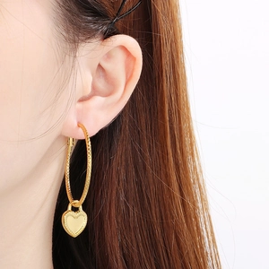 Fashionable gold heart charm hoop earrings worn by a model against a white background