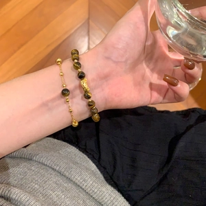 Close-up of 18K gold plated tiger eye bead bracelet set worn by a model holding a cup