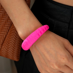 Nahaufnahme eines leuchtend rosa gewellten Acryl-Armreifs am Handgelenk mit Textur